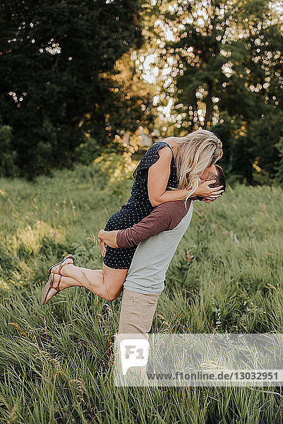 Romantischer Mann hebt seine Freundin auf einem Feld aus langem Gras hoch