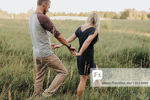 Romantic man and girlfriend strolling in field of sunlit long grass