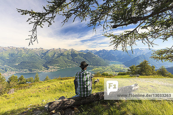 Man sitting on tree trunk looks towards Lake Como and Alto Lario  Monte Legnoncino  Lecco province  Lombardy  Italy