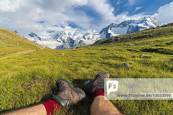 Hiker rests on grass looking towards Monte Rosa massif  Riffelalp  Zermatt  canton of Valais  Swiss Alps  Switzerland