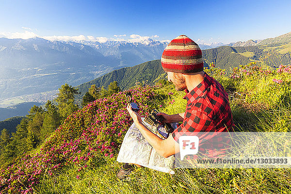Wanderer sitzt in der Nähe von Rhododendren auf dem Pizzo Berro und schaut auf den Kompass und die Karte  Bitto-Tal  Lombardei  Italien