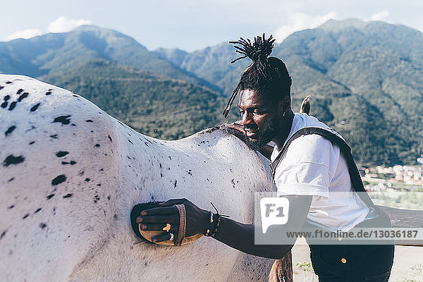 Cooler junger Mann pflegt Pferd in ländlicher Reitarena  Primaluna  Trentino-Südtirol  Italien