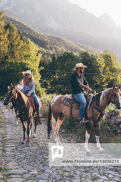 Erwachsene Freunde beim Reiten auf ländlicher Kopfsteinpflasterstraße  Primaluna  Trentino-Südtirol  Italien