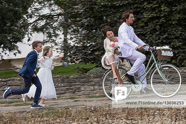 Junge Hochzeitsgäste rennen Neuvermählten auf Fahrrädern hinterher