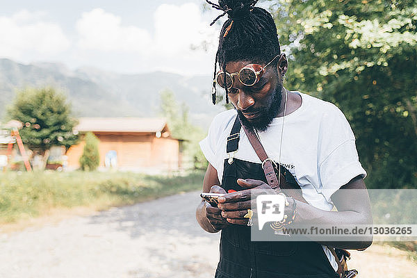 Cooler junger Mann auf ländlichem Feldweg mit Blick auf Smartphone  Primaluna  Trentino-Südtirol  Italien