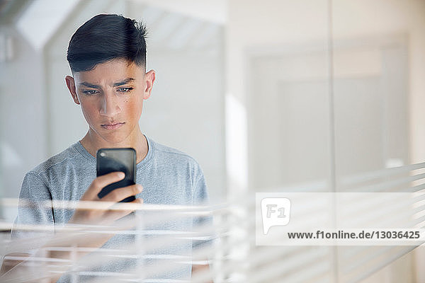 Teenager Junge liest Textnachricht auf Handy an Glaswand