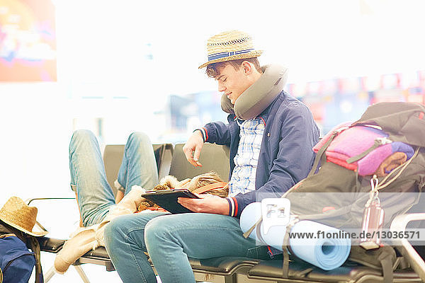 Junges Paar in der Abflughalle des Flughafens  Frau ruht Kopf auf den Beinen des Mannes  Mann benutzt digitales Tablett