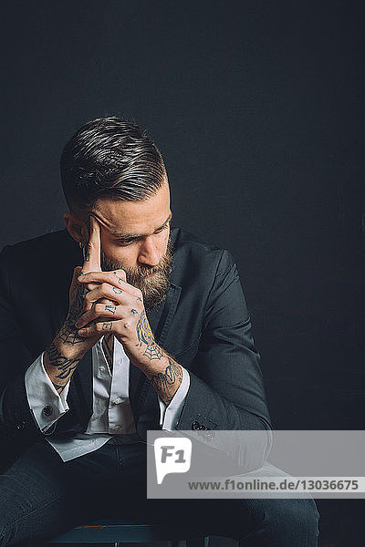 Young man wearing suit  sitting with worried expression  tattoos on hands