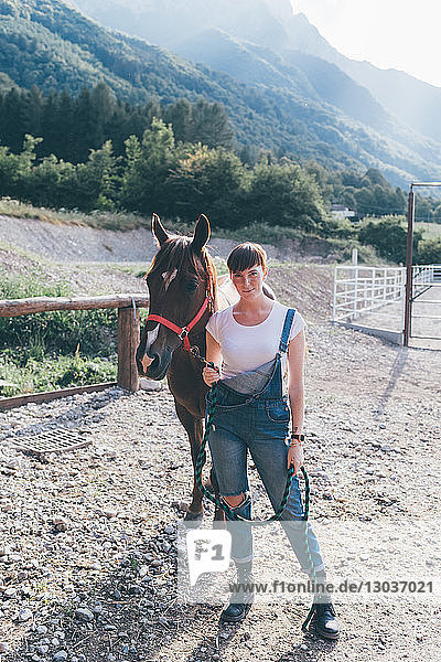 Junge Frau führt Pferd auf ländlichem Reitplatz  Ganzkörperporträt