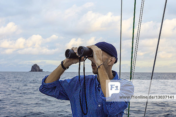 Kopf- und Schulteraufnahme eines Mannes  der durch ein Fernglas auf einem Segelboot im Meer schaut  Lombok  Indonesien