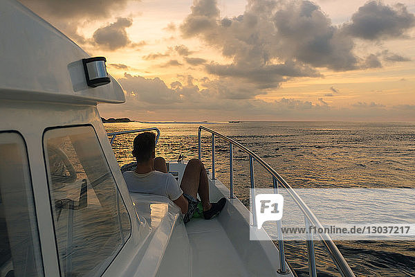 Rückansicht eines einzelnen männlichen Touristen auf einem Segelboot mit Blick auf die Aussicht bei Sonnenuntergang  Thulusdhoo  Male  Malediven