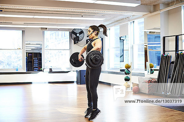 Seitenansicht einer einzelnen weiblichen Fitnesstrainerin  die im Fitnessstudio Gewichte hebt.