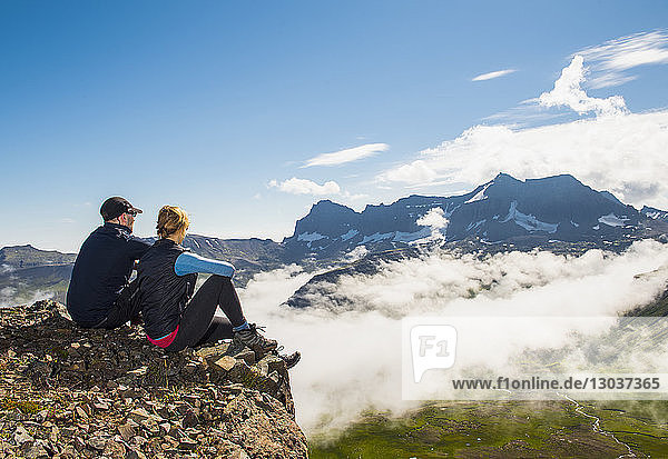 Ganzaufnahme eines Paares  das sitzt und den Blick auf die über dem Nebel aufsteigenden Berge genießt  Borgafjordur Eystri  Island