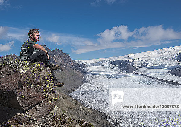 Seitenansicht eines männlichen Wanderers  der auf einem Felsen in der Nähe des Skaftafellsjokull-Gletschers sitzt  Vatnajokull-Nationalpark  Island