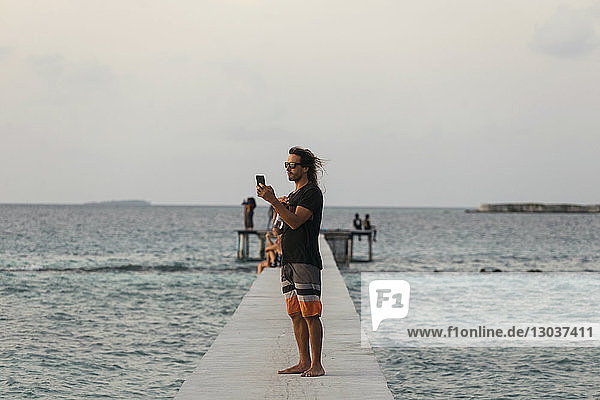 Seitenansicht eines einzelnen mÃ?nnlichen Touristen  der ein Foto auf einem Pier macht â€ Thulusdhoo  Male  Malediven