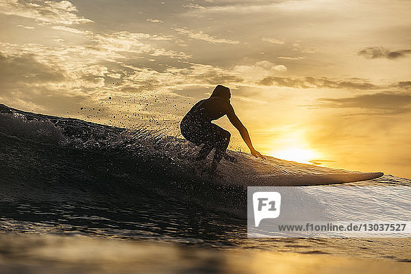 Silhouette eines mÃ?nnlichen Surfers  der bei Sonnenuntergang auf einer Welle im Meer reitet  Changgu  Bali  Indonesien