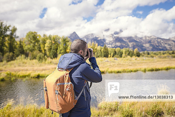 Man with backpack photographing while standing at riverbank