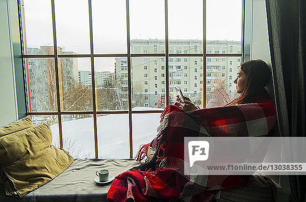 Frau in eine Decke gewickelt  während sie auf einem Fensterplatz in einer Nische sitzt