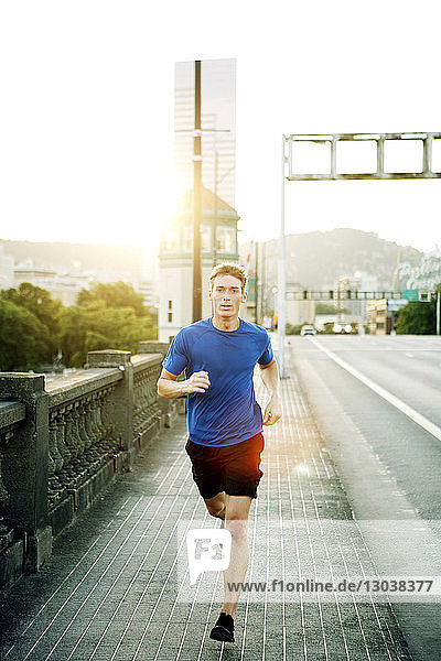 Portrait of sporty man jogging on footpath in city