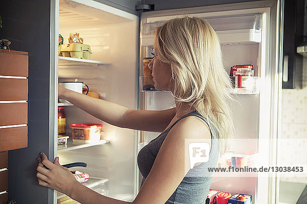 Seitenansicht eines Teenager-Mädchens  das im Kühlschrank in die Küche schaut