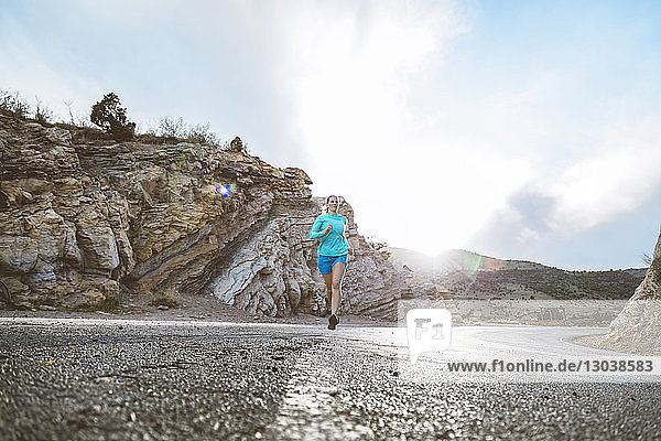 Entschlossene Sportlerin läuft bei Sonnenschein auf Landstraße gegen Felsen