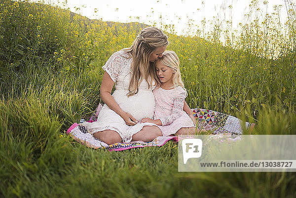Glückliche Mutter küsst Tochter auf die Stirn  während sie im Park sitzt