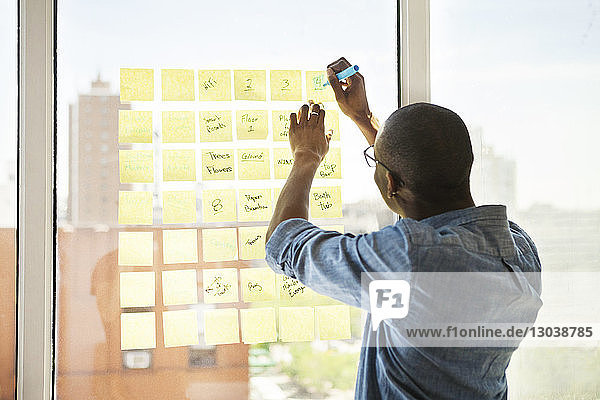 Rear view of businessman writing on adhesive note in creative office