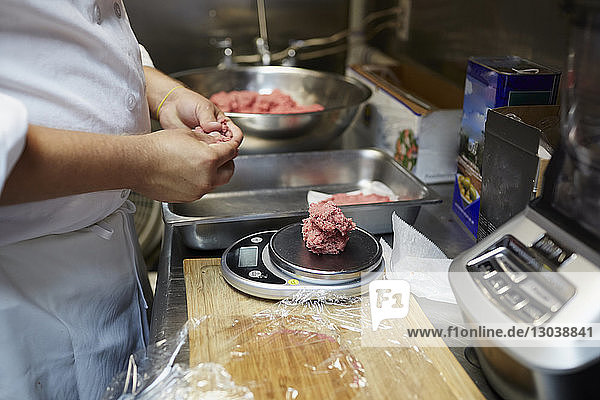 Midsection of chef measuring beef on weight scale in commercial kitchen