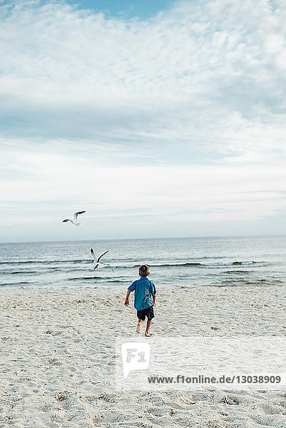 Rear view of boy running at Panama City Beach against cloudy sky