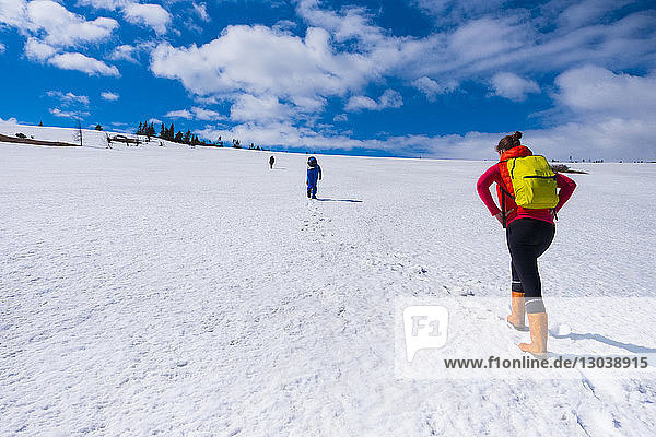 Rear view of hikers walking on snow covered field against cloudy sky