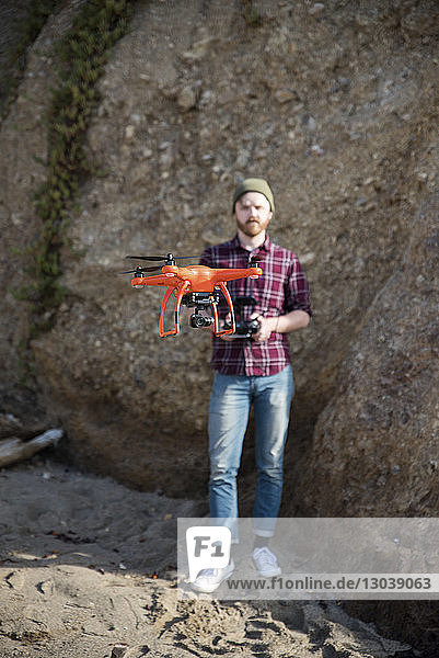 Full length of man flying drone while standing against rock formation