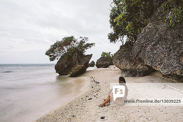 Seitenansicht eines an Felsen am Strand sitzenden Paares