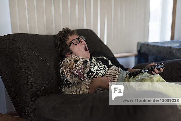 Boy and dog yawning while sitting on sofa at home