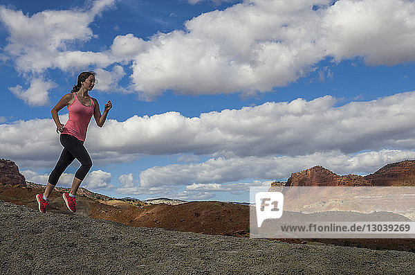 Athlete running on rock formations against cloudy sky