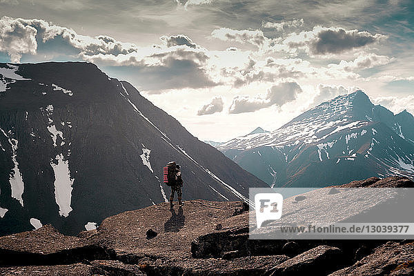 Rear view of hiker standing on cliff against snowcapped mountains