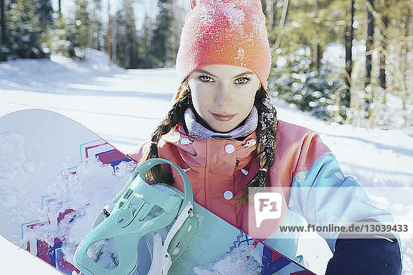 Porträt einer Frau  die im Winter im Wald stehend ein Snowboard hält