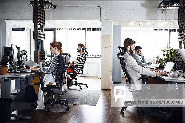 Side view of business people working at computer desks in creative office