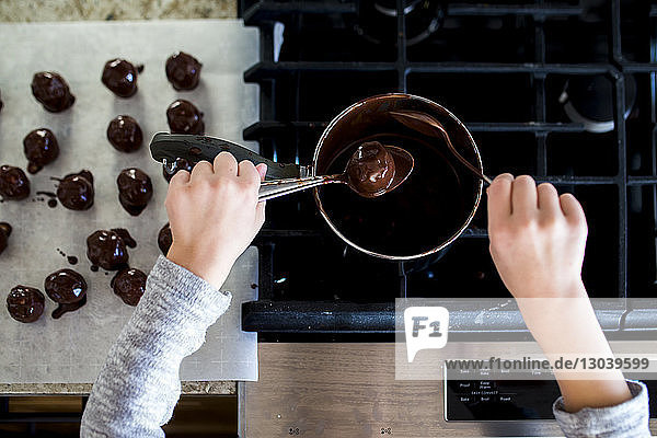 Abgetrennte Hände eines Mädchens  das zu Hause in der Küche Schokoladentrüffel herstellt