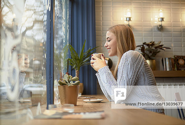 Seitenansicht einer Frau bei einem Drink am Tisch in einem Café