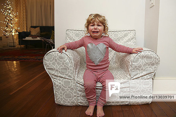 Portrait of girl crying while sitting on armchair at home