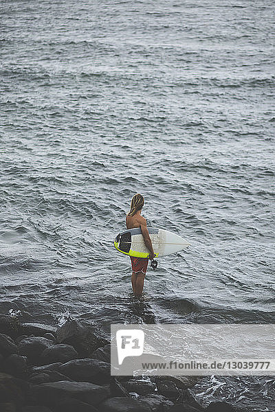 High angle view of man with surfboard standing in sea