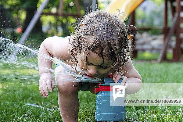 Playful girl drinking water from sprinkler in yard