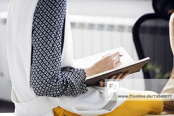 Midsection of businesswoman holding diary and pen in creative office