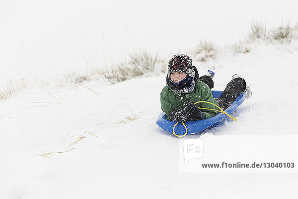 Teenage boy sledding on snow covered landscape during winter
