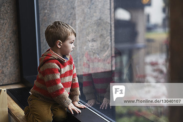 Boy looking through window while kneeling at home