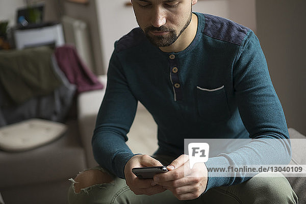 Mann benutzt Mobiltelefon  während er zu Hause auf dem Sofa sitzt