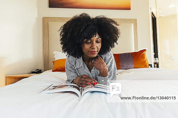 Geschäftsfrau liest Zeitschrift im Hotelzimmer im Bett liegend