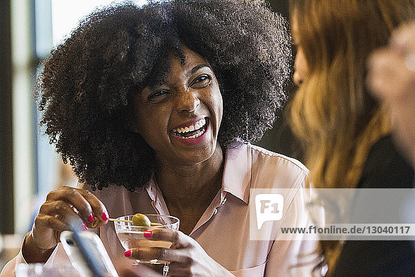 Fröhliche Geschäftsfrau hält Getränk in der Hand  während sie eine Kollegin im Hotel anschaut