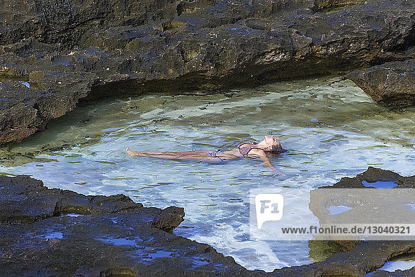 Woman wearing bikini lying in sea by rocks