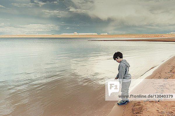 Side view of boy standing by Lake Powell against cloudy sky